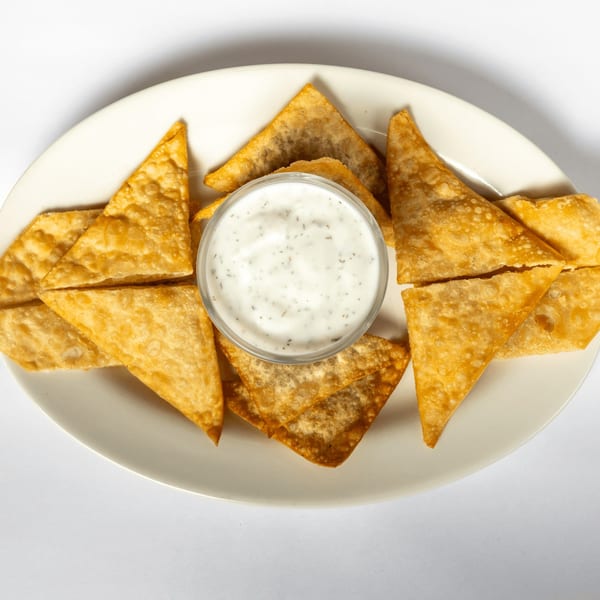 Crispy golden wonton triangles arranged around a small bowl of creamy white dipping sauce with herbs.
