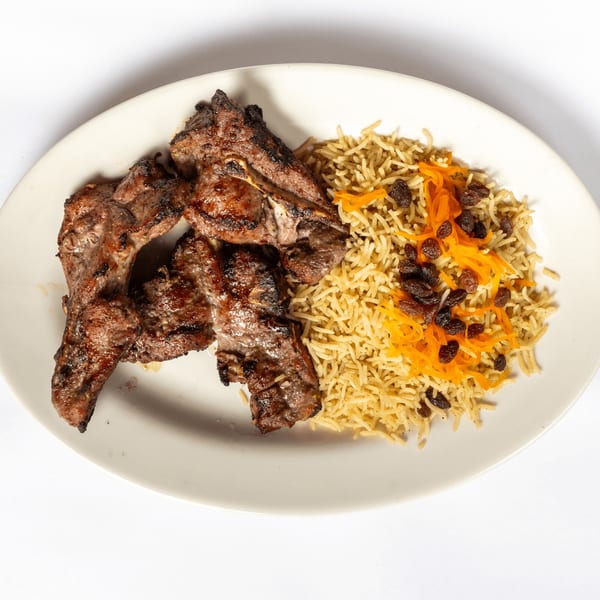 Grilled lamb chops with seasoned rice, topped with shredded carrots and raisins, on a white plate.