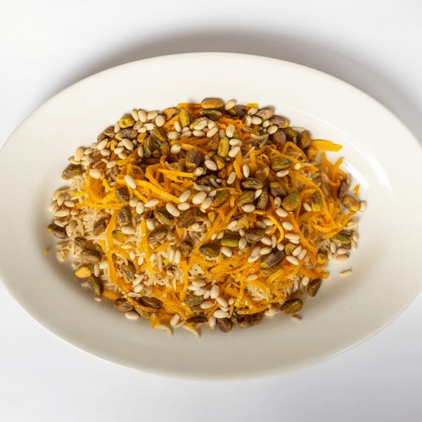 A white plate holds rice pilaf topped with shredded carrots, pine nuts, and pistachios.