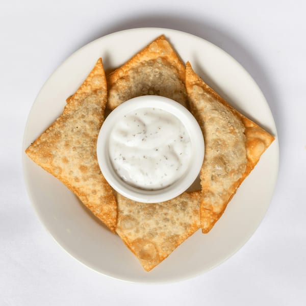 Four golden-brown fried wontons arranged around a small white bowl of creamy dipping sauce.