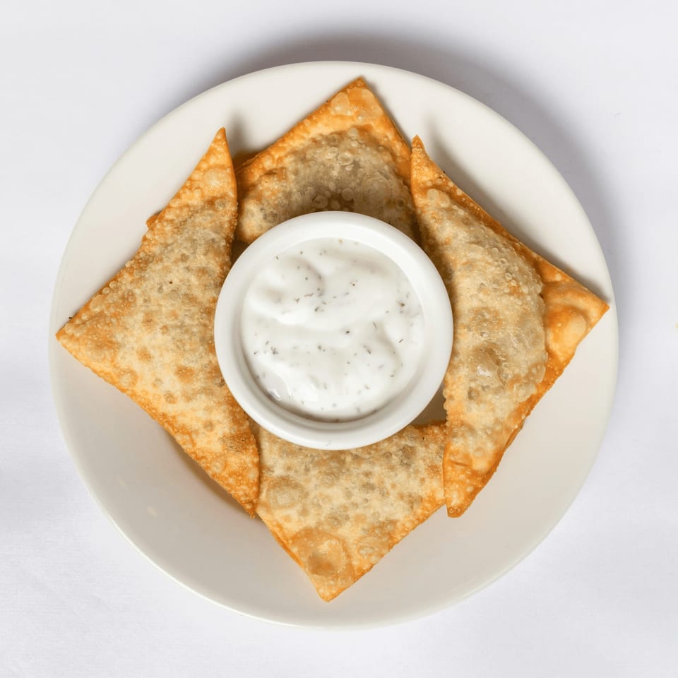 Four golden-brown fried wontons arranged around a small white bowl of creamy dipping sauce.