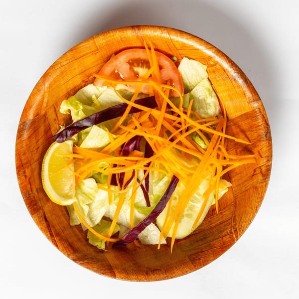 Overhead view of a fresh garden salad with lettuce, carrots, tomato, and lemon in a wooden bowl.