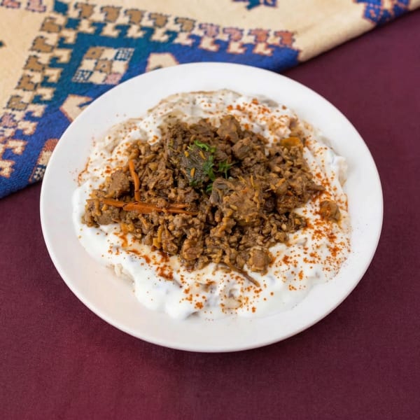 A white plate of ground meat and rice topped with yogurt and paprika, on a maroon tablecloth.