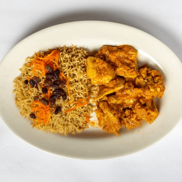 Chicken curry with rice, topped with shredded carrots and raisins, on a white oval plate.