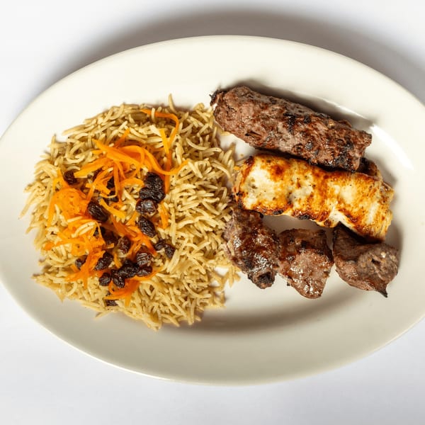 A white plate with rice pilaf topped with carrots and raisins, and three skewers of grilled meat.
