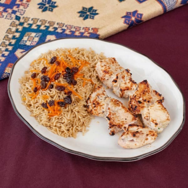 Grilled chicken pieces and rice with shredded carrots and raisins on a white plate.
