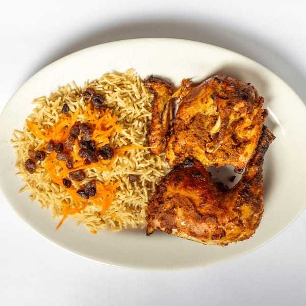A plate of roasted chicken and rice pilaf topped with shredded carrots and raisins.