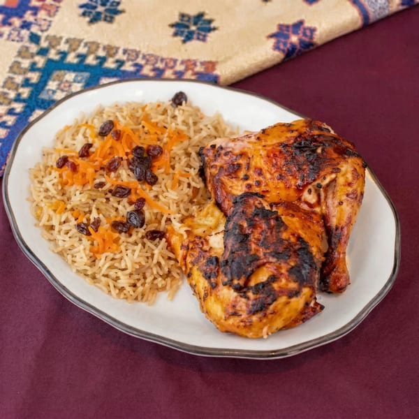 Grilled chicken pieces and rice with shredded carrots and raisins on a white plate.